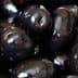 A close-up view of shiny black olives piled together in a cluster. - Olive Oil Times