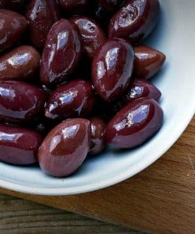 Bowl of Kalamata olives next to feta cheese on a wooden cutting board. - Olive Oil Times