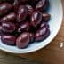 Bowl of Kalamata olives next to feta cheese on a wooden cutting board. - Olive Oil Times