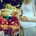 Pregnant woman standing in front of a fruit market display with various fruits. - Olive Oil Times
