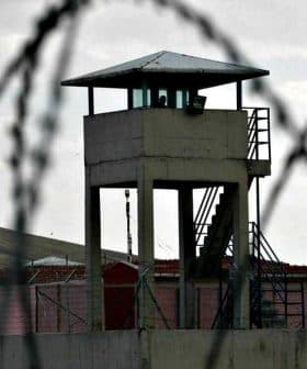 A prison watchtower surrounded by barbed wire fencing in a cloudy environment. - Olive Oil Times