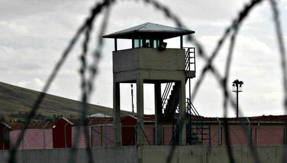 A prison watchtower surrounded by barbed wire fencing in a cloudy environment. - Olive Oil Times