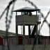 A prison watchtower surrounded by barbed wire fencing in a cloudy environment. - Olive Oil Times