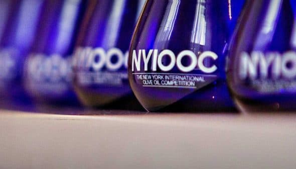 Blue glass awards with 'NYIOOC The New York International Olive Oil Competition' text displayed in a row. - Olive Oil Times