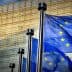 Three European Union flags waving in front of a modern glass building. - Olive Oil Times