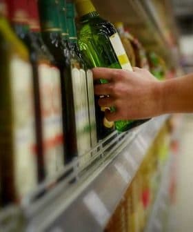 A person reaching for a green bottle of olive oil on a supermarket shelf. - Olive Oil Times