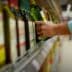 A person reaching for a green bottle of olive oil on a supermarket shelf. - Olive Oil Times