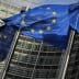 Multiple European Union flags waving in front of a modern glass building. - Olive Oil Times
