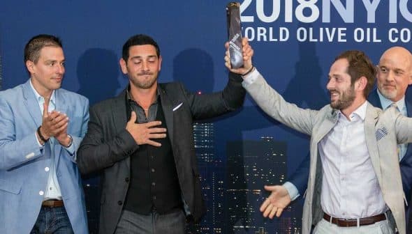 Four men at the 2018 New York Olive Oil Competition, one holding an award while others applaud. - Olive Oil Times