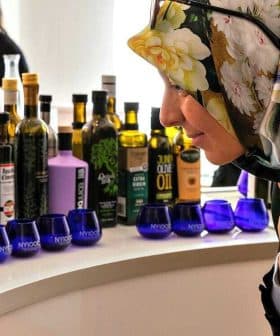 Woman wearing a floral headscarf examining various bottles of olive oil on display. - Olive Oil Times