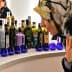 Woman wearing a floral headscarf examining various bottles of olive oil on display. - Olive Oil Times