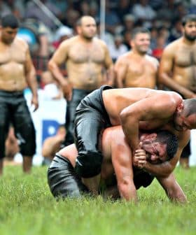 Two wrestlers engaged in a match on a grassy field with spectators in the background. - Olive Oil Times
