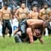 Two wrestlers engaged in a match on a grassy field with spectators in the background. - Olive Oil Times