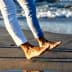 Two individuals walking barefoot along the shoreline with waves in the background. - Olive Oil Times