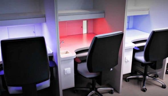 Four office workstations with ergonomic chairs and adjustable lighting in various colors. - Olive Oil Times