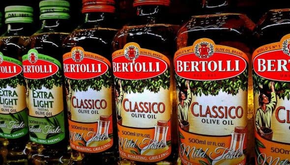 Row of Bertolli olive oil bottles in various types including Classico and Extra Light. - Olive Oil Times