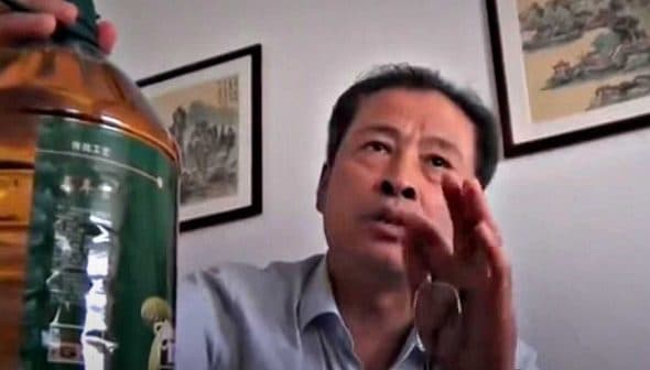 Individual holding a large plastic bottle of oil while speaking during a video call. - Olive Oil Times