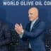 Two men at the World Olive Oil Competition award ceremony, one holding a trophy and the other applauding. - Olive Oil Times