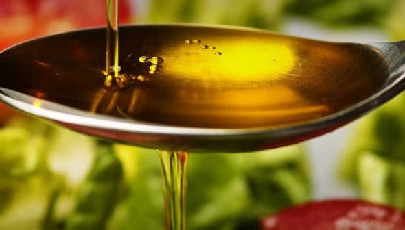 Close-up of a silver spoon holding olive oil above fresh vegetables on a plate. - Olive Oil Times