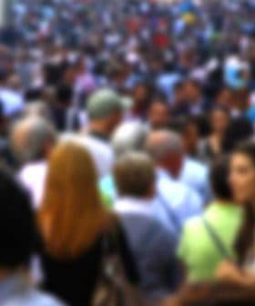 A blurred image showing a large crowd of people walking on a busy street. - Olive Oil Times
