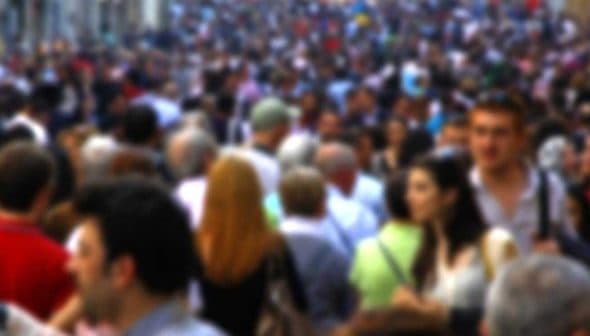 A blurred image showing a large crowd of people walking on a busy street. - Olive Oil Times