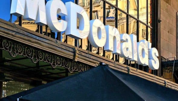 Signage of a McDonald's restaurant with reflective glass facade in the background. - Olive Oil Times