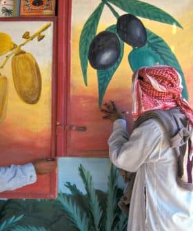 Two men in traditional attire examining wall murals depicting olives and dates. - Olive Oil Times