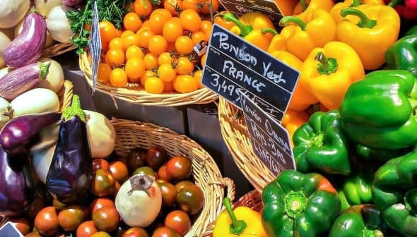 Variety of fresh vegetables including bell peppers, tomatoes, and eggplants arranged in baskets. - Olive Oil Times