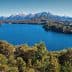 A panoramic view of a lake surrounded by mountains and forests under a clear blue sky. - Olive Oil Times