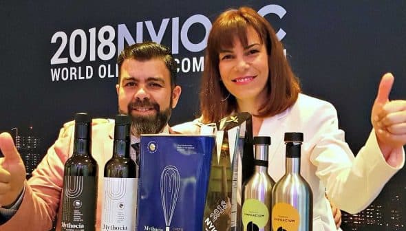 Two individuals giving thumbs up while posing with various olive oil bottles and awards. - Olive Oil Times