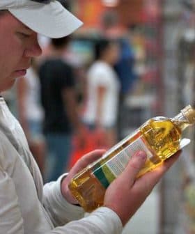 Individual inspecting a bottle of cooking oil while standing in a grocery store aisle. - Olive Oil Times