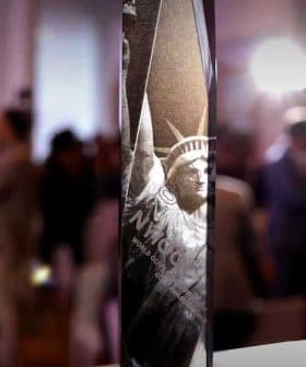 Statue of Liberty model displayed prominently at an indoor event with blurred background attendees. - Olive Oil Times