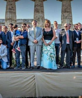 A large group of people posing for a photo in front of ancient columns at a historical site. - Olive Oil Times