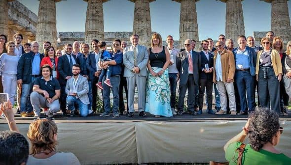 A large group of people posing for a photo in front of ancient columns at a historical site. - Olive Oil Times
