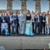 A large group of people posing for a photo in front of ancient columns at a historical site. - Olive Oil Times