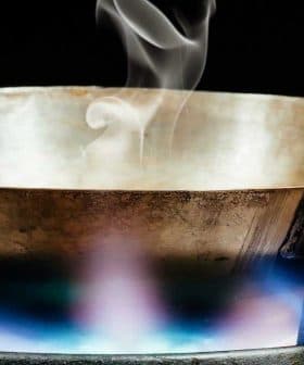 Metal cooking pan with steam rising above it on a gas stove with a blue flame. - Olive Oil Times