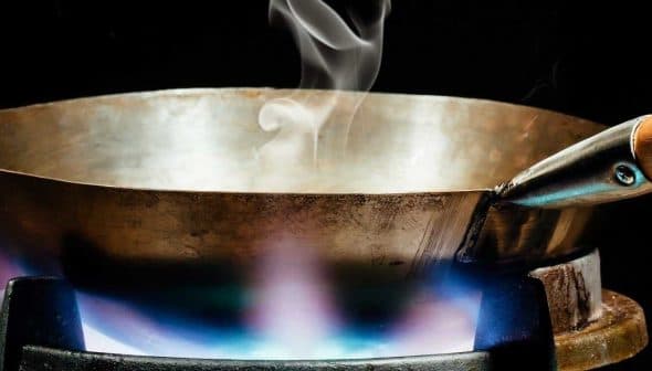 Metal cooking pan with steam rising above it on a gas stove with a blue flame. - Olive Oil Times