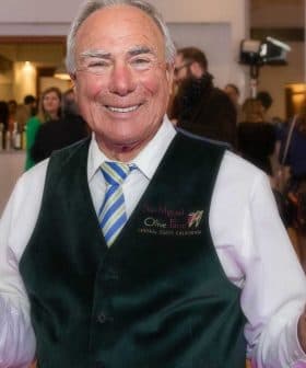 Man in a green vest holding an award and a bottle of olive oil at an event. - Olive Oil Times
