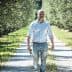 A man walking along a gravel path in an olive grove surrounded by trees. - Olive Oil Times