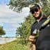 Man in sunglasses pouring olive oil from a bottle into a glass while standing among olive trees. - Olive Oil Times