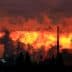 Silhouetted industrial structures emitting smoke against a vibrant sunset sky. - Olive Oil Times