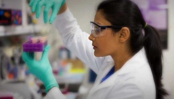 Female scientist in a lab coat and gloves handling samples in a laboratory setting. - Olive Oil Times