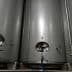 Three stainless steel fermentation tanks with circular openings and valves. - Olive Oil Times