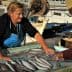 A woman in an apron selling fish at a market while a man points at the fish on display. - Olive Oil Times