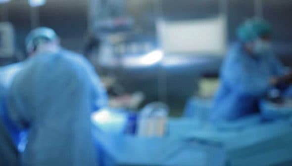 Two medical professionals wearing scrubs and masks working in an operating room with surgical instruments. - Olive Oil Times