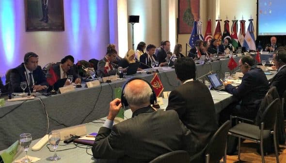 A conference room with delegates seated around a large table during a meeting. - Olive Oil Times