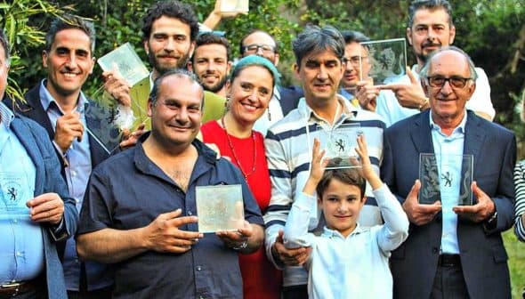 A group of individuals holding glass awards, posing together outdoors in a celebratory manner. - Olive Oil Times