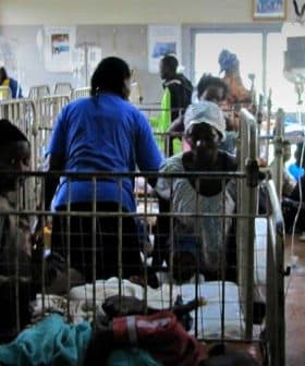 A hospital ward filled with patients in beds and medical staff attending to them. - Olive Oil Times