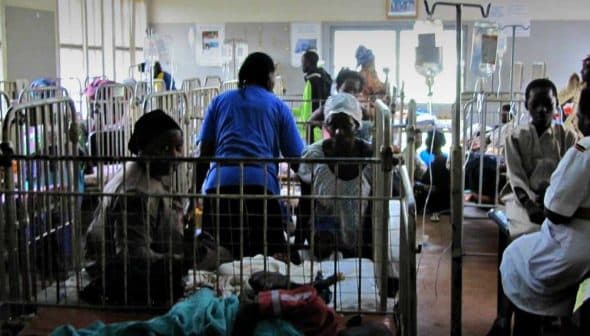 A hospital ward filled with patients in beds and medical staff attending to them. - Olive Oil Times