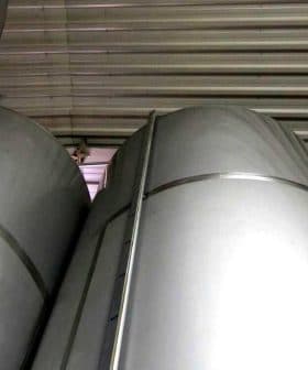 Several large silver storage tanks stacked closely together in a warehouse setting. - Olive Oil Times